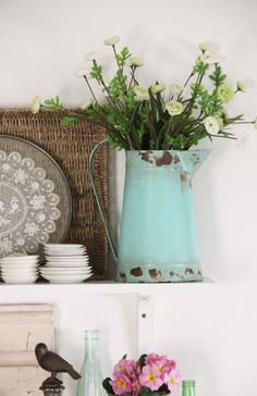 some flowers are in a blue vase on a shelf next to plates and other items