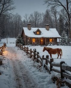 a horse is standing in the snow by a fence and cabin at night with lights on