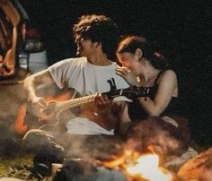 a man and woman sitting next to each other on the ground with a guitar in front of them