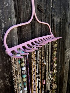 a pink metal rack with many necklaces hanging from it's sides and attached to a wooden wall