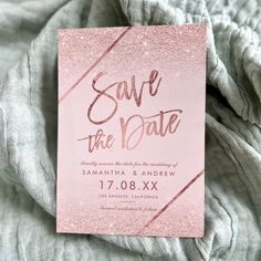 the save the date card is laying on top of a gray blanket with pink glitter