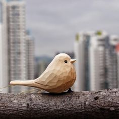 a wooden bird sitting on top of a tree branch in front of some tall buildings