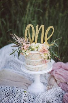 a cake sitting on top of a white plate covered in flowers and the word one