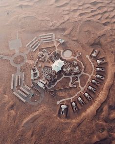 an aerial view of some buildings in the middle of dirt land with cars parked around it