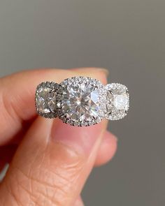 three stone diamond ring being held by someone's hand in front of the camera