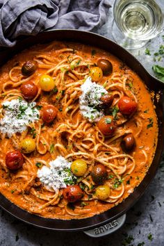 a pan filled with pasta topped with tomatoes and parmesan cheese on the side