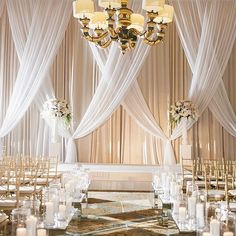 an elegant wedding set up with white drapes, candles and floral centerpieces