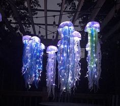 several jellyfish lights hanging from the ceiling in a dark room with trees behind them