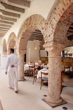 a man in white is walking through an archwayed dining room with tables and chairs