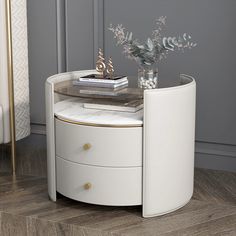 a white round table with two drawers and a glass vase on the top, in front of a gray wall