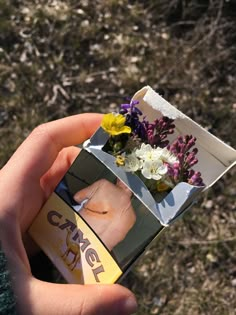 someone is holding a small box with flowers in it and there are other things inside