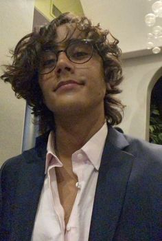 a man with curly hair wearing glasses and a suit jacket is looking off to the side