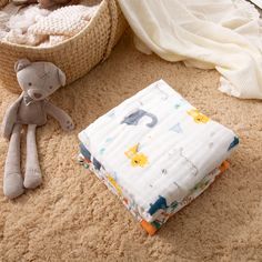 a teddy bear sitting on the floor next to a blanket and stuffed animal in a basket