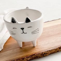 a white cat shaped bowl sitting on top of a wooden table next to a towel