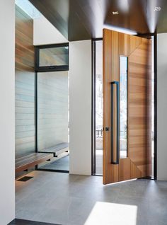 an empty room with a wooden door and bench in the center, surrounded by glass doors