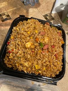 a container filled with rice and vegetables on top of a tiled counter next to plastic containers