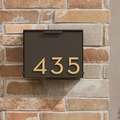 a house number sign mounted to the side of a brick wall with gold numbers on it