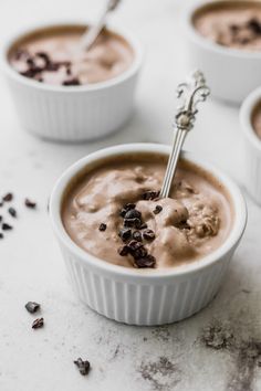 three white bowls filled with chocolate pudding on top of a table next to spoons