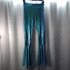 a pair of blue and green mermaid pants hanging on a wall with curtains behind it