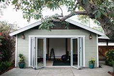 a garage with sliding glass doors on the front and side walls, surrounded by trees