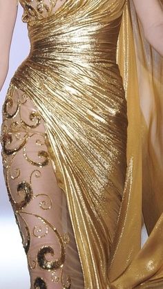 a woman in a gold dress walking down the runway with her hand on her hip