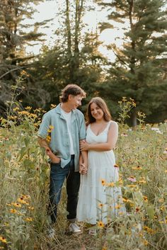 a man and woman standing in the middle of a field full of wildflowers