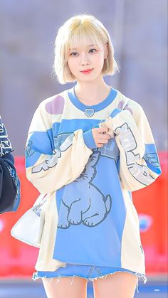 a girl with short blonde hair wearing a blue and white shirt is walking down the street