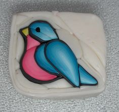 a blue and pink bird sitting on top of a white square tile wall hanging ornament