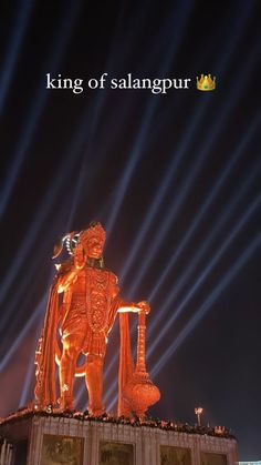 the statue is lit up at night with light streaks in the sky behind it and on top of a building