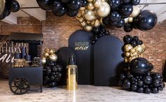 black and gold balloons are hanging from the ceiling in front of a table with an empty bottle on it