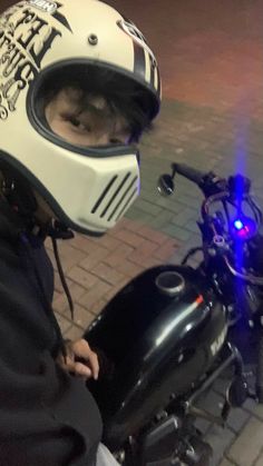 a person wearing a helmet and sitting on a motor bike with its lights on at night