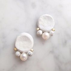 two white and green earrings on a marble surface with gold studded ear wires,