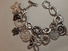 This sale is for a heave and chunky charm bracelet that is designed in silver tone metal. The cable link chain is decorated with fifteen charms that include loops, square shapes, spiral shapes, and flowers. The length of the bracelet is 9" and it fastens with an interlocking bar and loop.  The silver tone finish is in excellent condition. Chunky Silver Bracelet, Chunky Charm Bracelet, Bracelet With Charms, Chunky Bracelet, Spiral Shape, Metal Charms, Sterling Silver Charm Bracelet, Chunky Bracelets, Toggle Bracelet