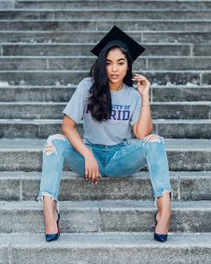 a woman sitting on some steps wearing a graduation cap and ripped blue jeans with her legs crossed