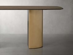 a modern dining table with an oval shaped base in gold and brown wood, against a gray background