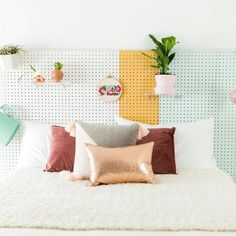 a white bed topped with lots of pillows next to a wall mounted potted plant