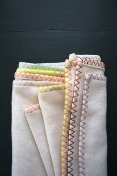 four pieces of white fabric with orange, yellow and green stitching on the edges