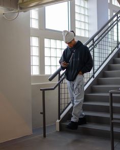 a man standing at the bottom of stairs looking at his cell phone while using it