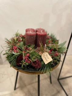 two candles are sitting on a table with evergreen and berries