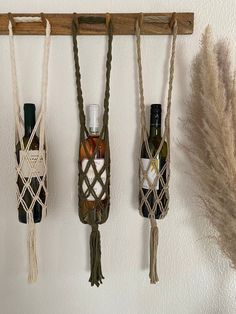 three bottles of wine are hanging on the wall with rope wrapped around them and some feathers