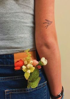 a woman with a small tattoo on her left arm and flowers in her pocket behind her back