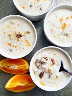 four white bowls filled with food next to sliced oranges and an apple on the side