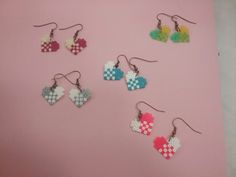 six pairs of heart shaped earrings hanging from hooks on a pink background with white and blue squares