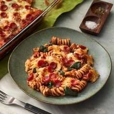 a plate of pasta with pepperoni and spinach on it next to a casserole dish