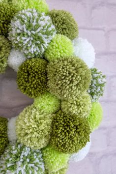 a green and white wreath with pom - poms hanging on a brick wall