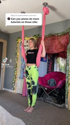 a woman is standing on one leg and holding two pink poles in the other hand, with a sign above her head that says can you pizza do more turlials on these silks