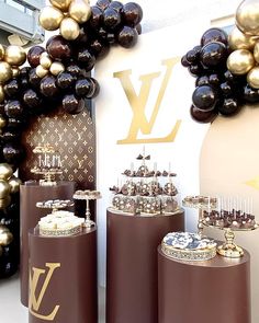 a table topped with lots of chocolate covered cakes next to balloons in the shape of louis vuittons