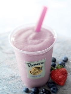 a pink smoothie in a plastic cup with a straw and blueberries on the side