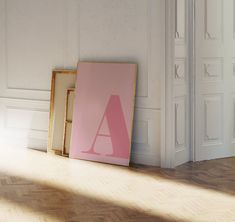 an empty room with two frames on the floor and a pink letter next to it