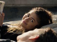 a woman laying on the ground reading a book with her eyes wide open and looking at the camera